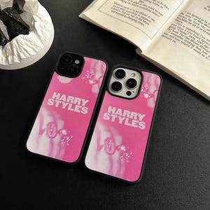 May include: Two black iPhone cases with a pink and white design featuring the text "HARRY STYLES".
