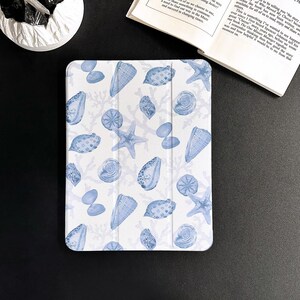 May include: A white iPad case featuring a blue and white seashell pattern. The case has a textured surface and is designed to protect the iPad.