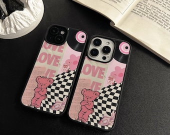 May include: Two phone cases with a pink and black design. The cases feature the word "LOVE" in pink, a pink teddy bear, a checkerboard pattern, and a vinyl record design. The cases are black.