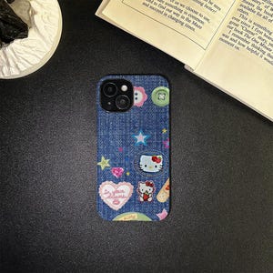May include: A blue denim iPhone case with a variety of colorful patches and embellishments, including a Hello Kitty character, stars, hearts, and a button. The text "In your dreams" is on a pink heart patch.