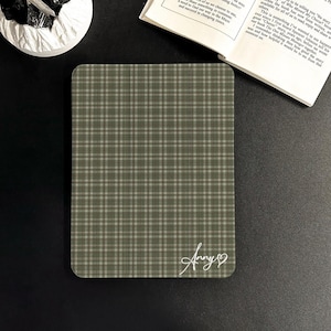Peut inclure: Un dessous de verre rectangulaire à motif de carreaux verts et beiges avec des coins arrondis. Le dessous de verre porte une signature manuscrite "Anny" avec un symbole de cœur. Le dessous de verre est sur une surface noire.