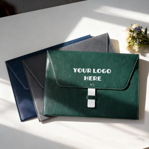 May include: Three document holders in navy, grey, and green. The green one has the text "YOUR LOGO HERE" in white. Each has a flap closure with white stitching and a white clasp. Ideal for office or school.