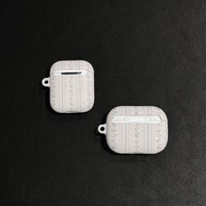 May include: Two white AirPod cases with a floral pattern and a small loop for a keychain. The cases have a rectangular shape with rounded edges and a small opening at the top.