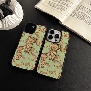 May include: Two phone cases with a green background featuring a repeating pattern of brown teddy bears, cherries, and watermelon slices. The cases have black borders and are likely for smartphones.