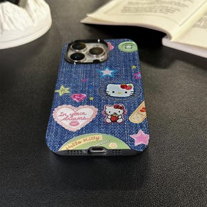 May include: A blue denim phone case with Hello Kitty and other cartoon characters, including a heart with the text "In your dreams".