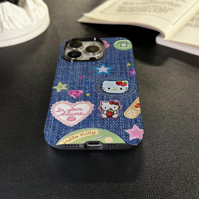 May include: A blue denim phone case with Hello Kitty and other cartoon characters, including a heart with the text "In your dreams".
