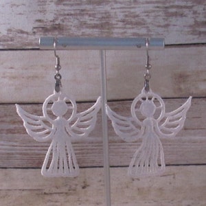 May include: A pair of white angel-shaped earrings hanging from a silver earring stand. The earrings are made of delicate white lace and have a halo around the head.