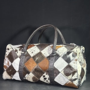 May include: A brown leather duffel bag with a patchwork design of different coloured cowhide. The bag has two top handles and a zip closure.