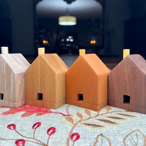 May include: Four wooden houses in different shades of brown, beige, and reddish brown. Each house has a small chimney on top and a rectangular opening for a door.