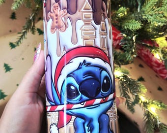 Op de afbeelding: Een roestvrijstalen beker met een feestelijk ontwerp. Het heeft een stripfiguur met een kerstmuts en een zuurstok. De achtergrond heeft peperkoekmannetjes en een chocoladedruipontwerp. De beker is ongeveer 15 cm hoog.