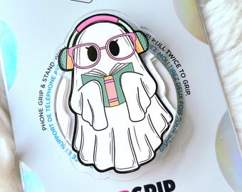 Op de afbeelding: Een witte PopSocket telefoonhouder met een cartoon spook met een roze bril en koptelefoon, lezend in een boek. De PopSocket zit op een witte achtergrond met de woorden "POPSOCKETS" en "POPGRIP".