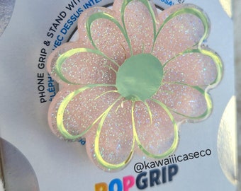 Op de afbeelding: Een roze en groene glitter telefoonhouder met een madeliefje ontwerp. De houder is gelabeld met "POPGRIP" en "@kawaiiicaseco".