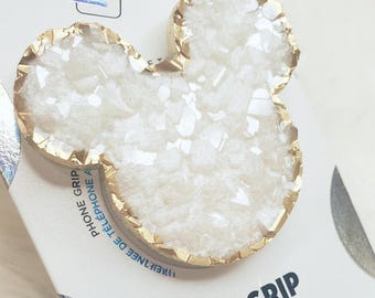 Op de afbeelding: Een wit en goudkleurig PopGrip telefoonaccessoire in de vorm van een muizenkop. Het accessoire heeft een goudkleurige rand en een wit, getextureerd midden. De PopGrip staat op een witte kaart met het woord "PopGrip" in kleurrijke letters.