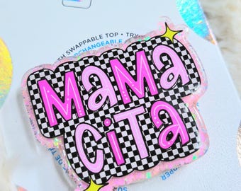 Op de afbeelding: Een roze en zwarte PopSocket met de tekst "Mama Cita" in een bubbellettertype. De achtergrond is een zwart-wit geblokt patroon. De PopSocket heeft een glitterrand en gele steraccenten.