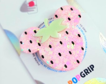 Op de afbeelding: Een roze aardbei PopSocket met zwarte zaden en een lichtgroene steel. De PopSocket heeft een glittertextuur en is bevestigd op een witte achterkant met het woord "POPGRIP" in oranje en zwart.