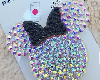 Op de afbeelding: Een transparante, iriserende PopSocket-telefoonhouder met een zwarte strik, met de tekst "POPGRIP PREMIUM" op de verpakking.