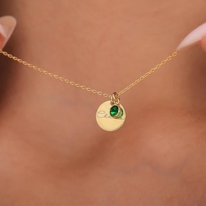 May include: Gold necklace with a round pendant engraved with the name "Ellie" and two small green gemstones.