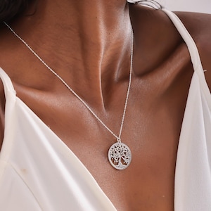 May include: A silver necklace with a tree of life pendant. The pendant is a circular design with a detailed tree silhouette.