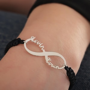 May include: A black cord bracelet with an infinity symbol charm. The charm has the names "Kevin" and "Karen" engraved on it.