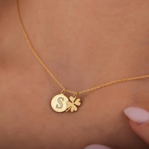 May include: A gold chain necklace with a round pendant featuring the letter "S" and a four-leaf clover charm.