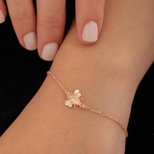 May include: A delicate gold chain bracelet with a small bee charm. The bee is detailed with wings and a body.
