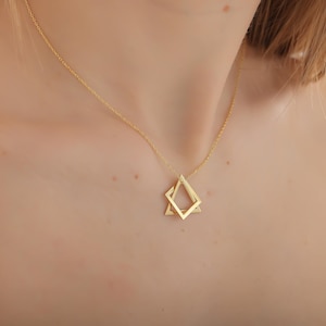 May include: A gold necklace with a geometric pendant featuring two overlapping shapes: a square and a triangle.