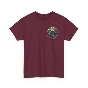 Puede incluir: Camiseta burdeos con un gráfico circular de un buey almizclero. El gráfico incluye la palabra "MUSKOX" y otro texto. La camiseta está hecha de un material suave y tiene mangas cortas.