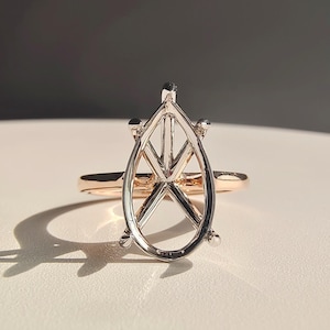 Könnte beinhalten: Eine Ringfassung mit einem silberfarbenen, birnenförmigen Korb mit Kreuzsteg-Design, montiert auf einem dünnen Roségold-Ringband. Die Fassung ist für einen einzelnen Edelstein ausgelegt und hat vier kleine Krappen an den oberen und unteren Kanten.