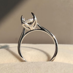 May include: A silver engagement ring with a prong setting. The ring features a small, clear gemstone held by four prongs. The band is smooth and polished, and the ring is set against a neutral background.