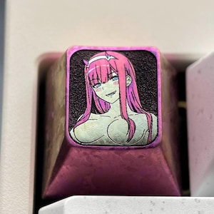 May include: A pink and purple keyboard keycap with a printed image of an anime character with pink hair. The keycap is on a white keyboard with the keys "Tab" and "Q" visible.