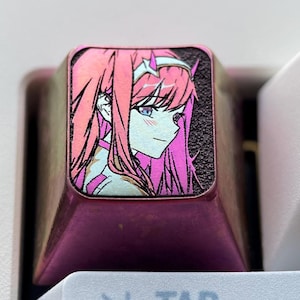 May include: A pink and purple keyboard keycap with a printed image of an anime character with pink hair. The keycap is labeled "TAB" and is surrounded by other white keyboard keys.