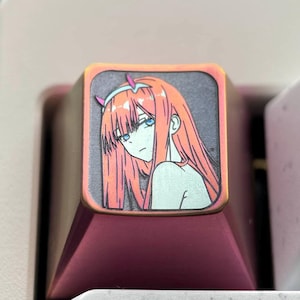 May include: A pink and copper mechanical keyboard keycap with a printed image of an anime character with red hair. The character is wearing a white outfit and has a red headband. The keycap is labeled with the word "Tab".