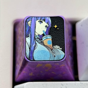 May include: A custom purple keycap with an anime-style illustration of a woman drinking from a beverage cup. The keycap is part of a white keyboard, with other keys labeled "Tab", "1", and "Q".