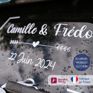 Peut inclure: Autocollant en vinyle blanc avec le texte "Camille & Frédo" et "22 Juin 2024" avec un cœur et une flèche. L'autocollant est sur une vitre de voiture noire.