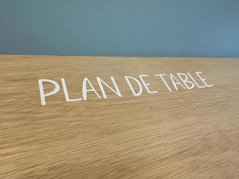 May include: A close-up of a wooden sign with the text "PLAN DE TABLE" written in white lettering.