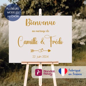 Peut inclure: Panneau de bienvenue blanc sur chevalet en bois, avec inscription dorée « Bienvenue au mariage de Camille & Frédo » et la date du « 22 juin 2024 ». Le panneau comporte également un logo et le texte « Fabriqué en France ».