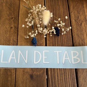 May include: A light blue sticker with the text "PLAN DE TABLE" in white lettering.