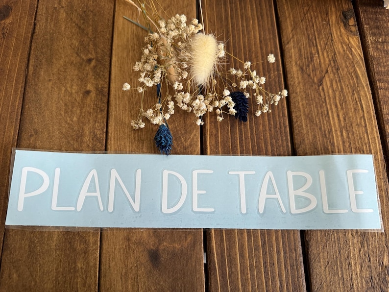 May include: A light blue sticker with the text "PLAN DE TABLE" in white lettering.