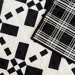 May include: Black and white quilt with a geometric pattern. The quilt is made of squares and diamonds, and the pattern is repeated throughout the quilt. The quilt is edged with a black fabric.