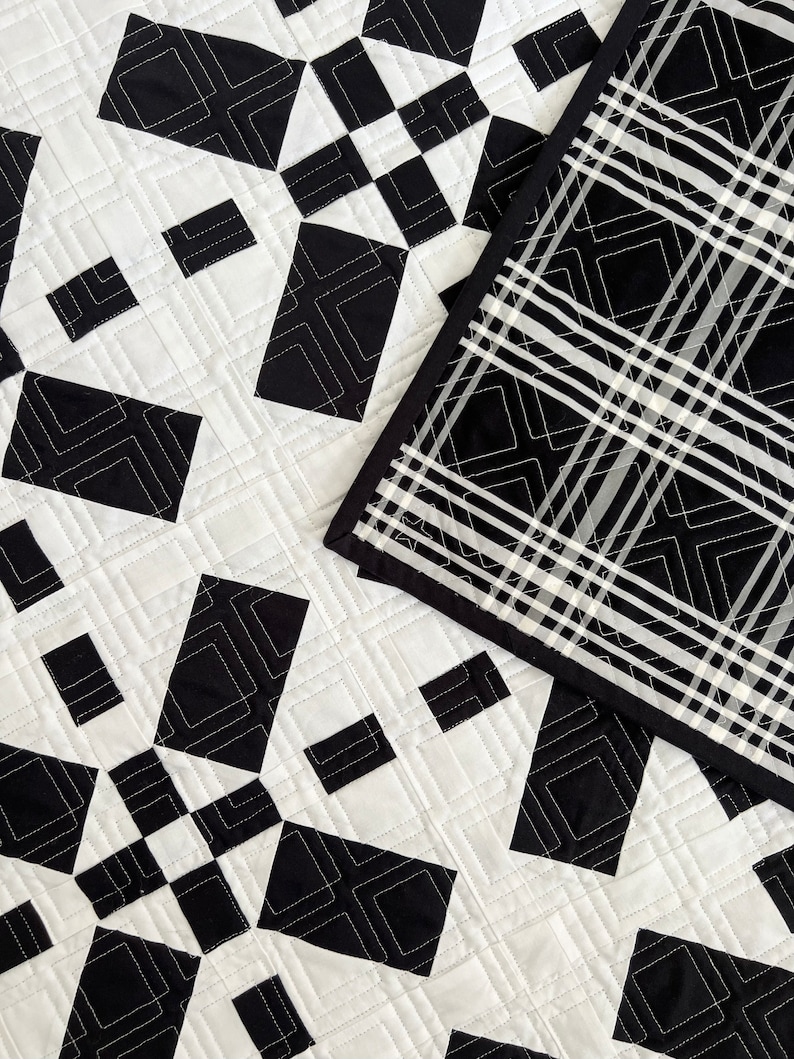 May include: Black and white quilt with a geometric pattern. The quilt is made of squares and diamonds, and the pattern is repeated throughout the quilt. The quilt is edged with a black fabric.