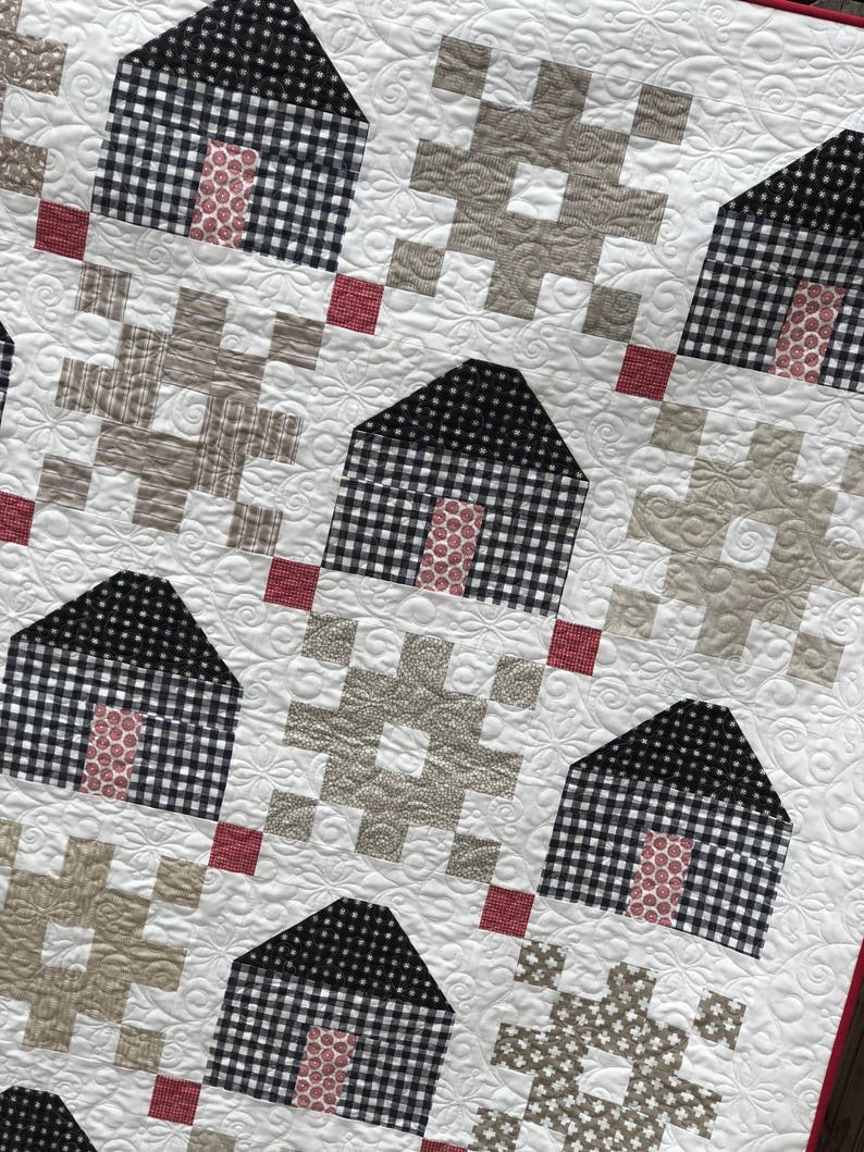May include: A quilt with a patchwork design featuring black and white gingham squares, red squares, and beige squares. The quilt is quilted with a floral pattern.