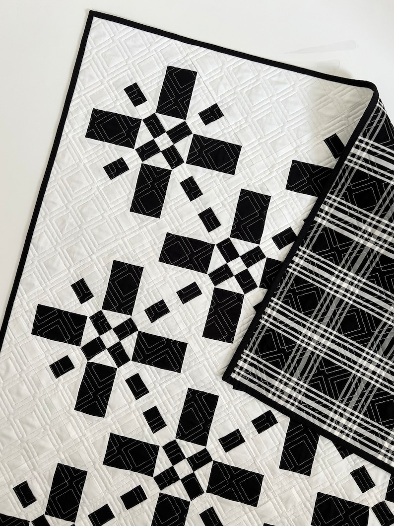 May include: Black and white quilt with a geometric pattern. The quilt is made of squares and rectangles, and the pattern is repeated throughout the quilt. The quilt is folded in half, and the back of the quilt is a black and white plaid.