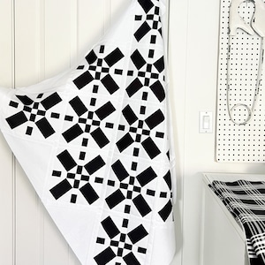 May include: A white fabric quilt with a black and white geometric pattern. The quilt is folded in half and hanging on a white door.