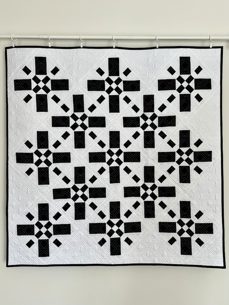 May include: A black and white quilt with a geometric pattern of stars. The quilt is hanging on a white wall.