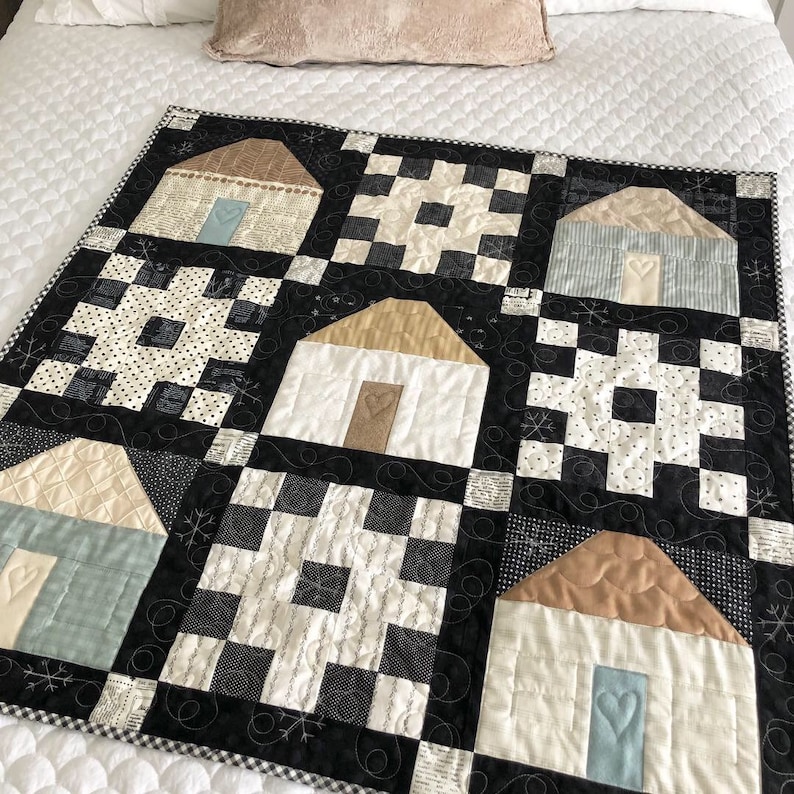 May include: A black and white quilt with a patchwork design featuring houses with brown roofs and blue doors. The quilt is made up of squares with different patterns, including checkered, polka dot, and floral.