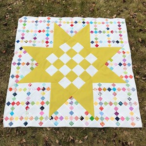 May include: A yellow and white quilt with a large yellow star in the center. The star is surrounded by a border of small colorful squares.
