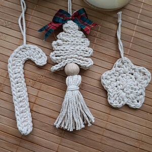 Puede incluir: Tres adornos de macramé hechos a mano: un árbol de Navidad con un lazo de tartán rojo y verde, una estrella y un bastón de caramelo. Los adornos están hechos con cordón de algodón beige natural y tienen un estilo rústico y de granja.