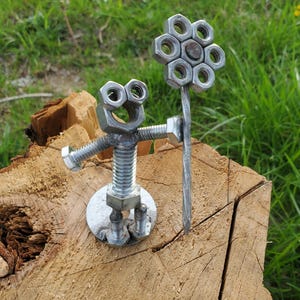May include: A metal sculpture of a person holding a flower made of nuts and bolts. The sculpture is standing on a wooden stump.