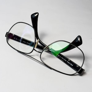 Op de afbeelding: Bril met zwart montuur en een dubbele brug. De binnenkant van de poot bevat de tekst PRADA Made in Italy R CE, terwijl de andere poot het modelnummer SPR 52P 61015 7AX-0A7 140 3N toont. De glazen zijn transparant.