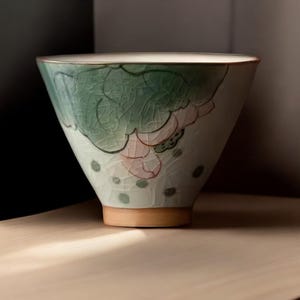 May include: A white ceramic bowl with a green and pink floral design. The bowl has a wide rim and a rounded bottom.